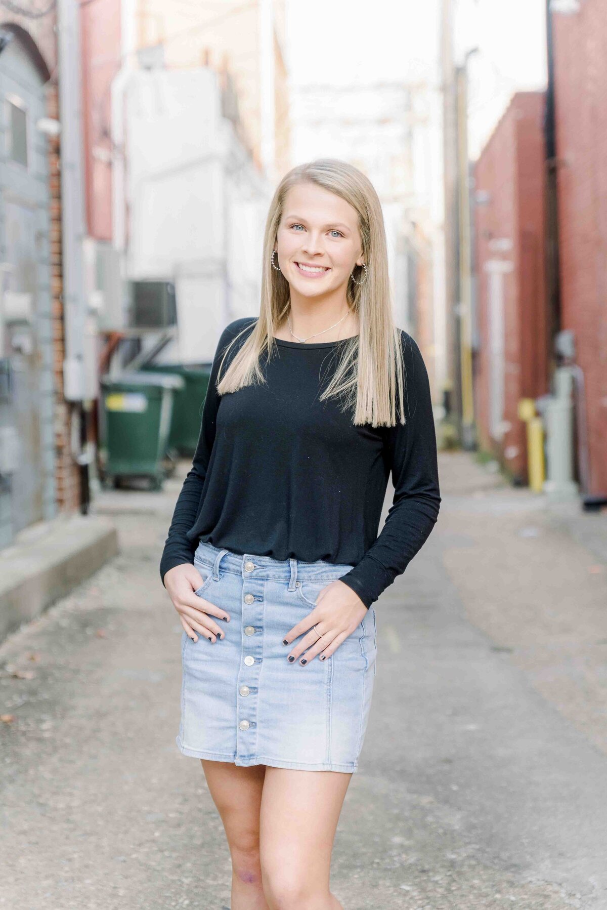 senior girl wearing a jean skirt and black shirt standing in the alley way