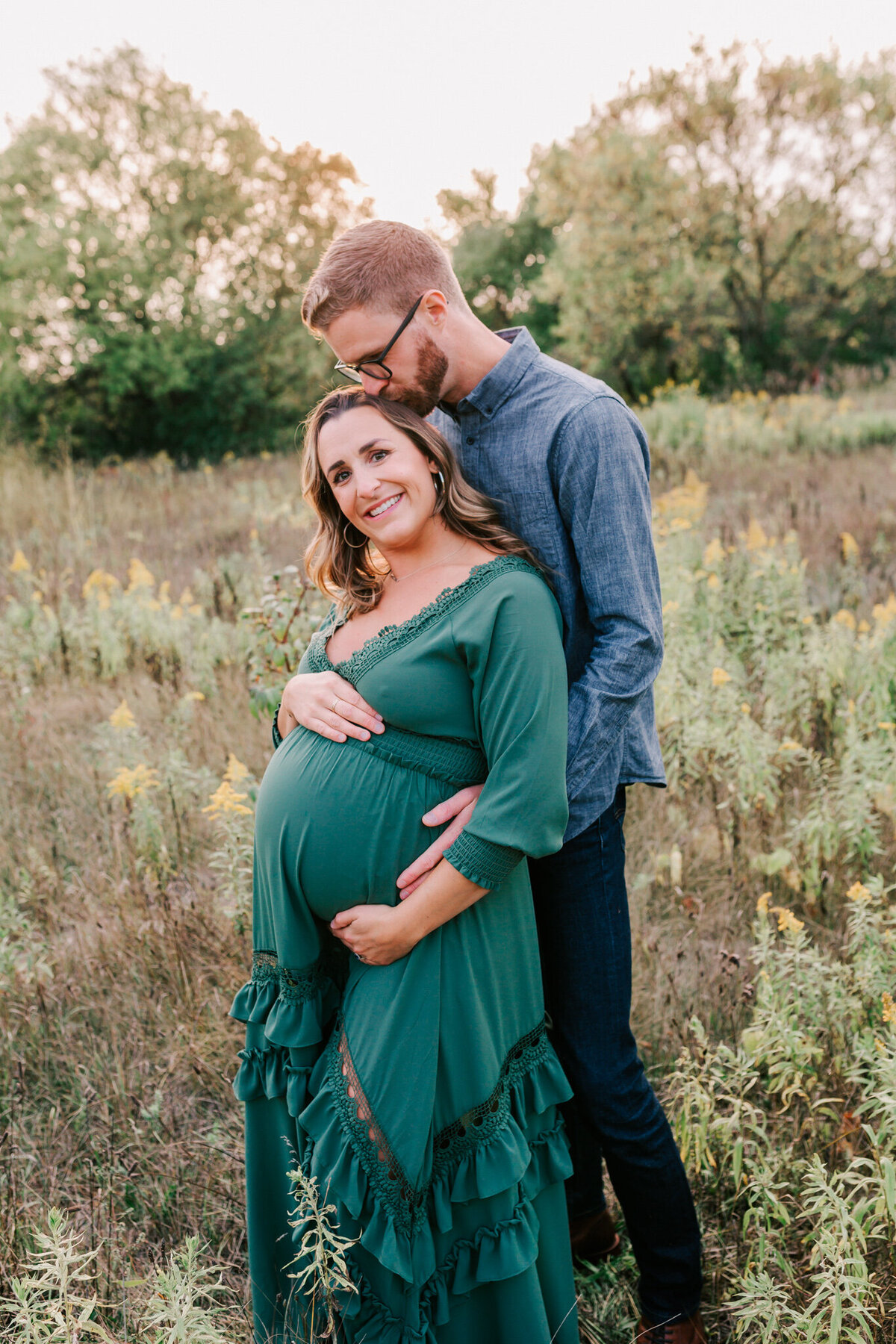 Father kisses mom on the head while in the field during her Maternity Session.