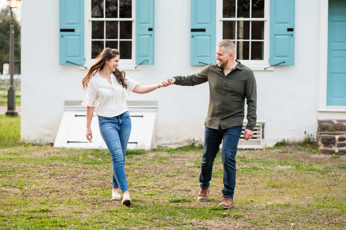 A man and woman walk hand in hand outside a light-colored building with blue shutters.