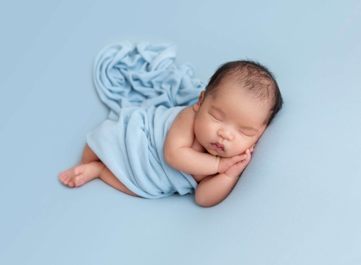 A sweet newborn baby boy swaddled in a soft blue wrap, taken in a Manhattan newborn photography session