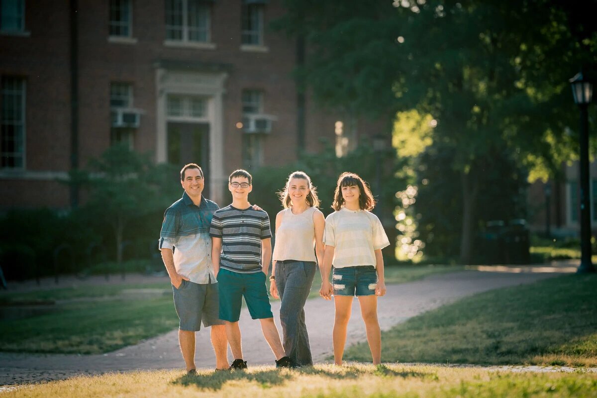 A family of four standing on a grassy quad.