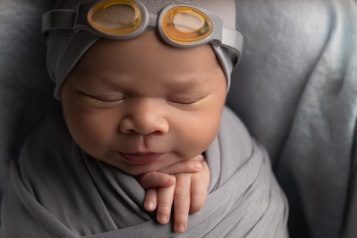 Fun newborn photography with baby wearing swim goggles and wrapped in gray, captured by Dallas Newborn Photographer.