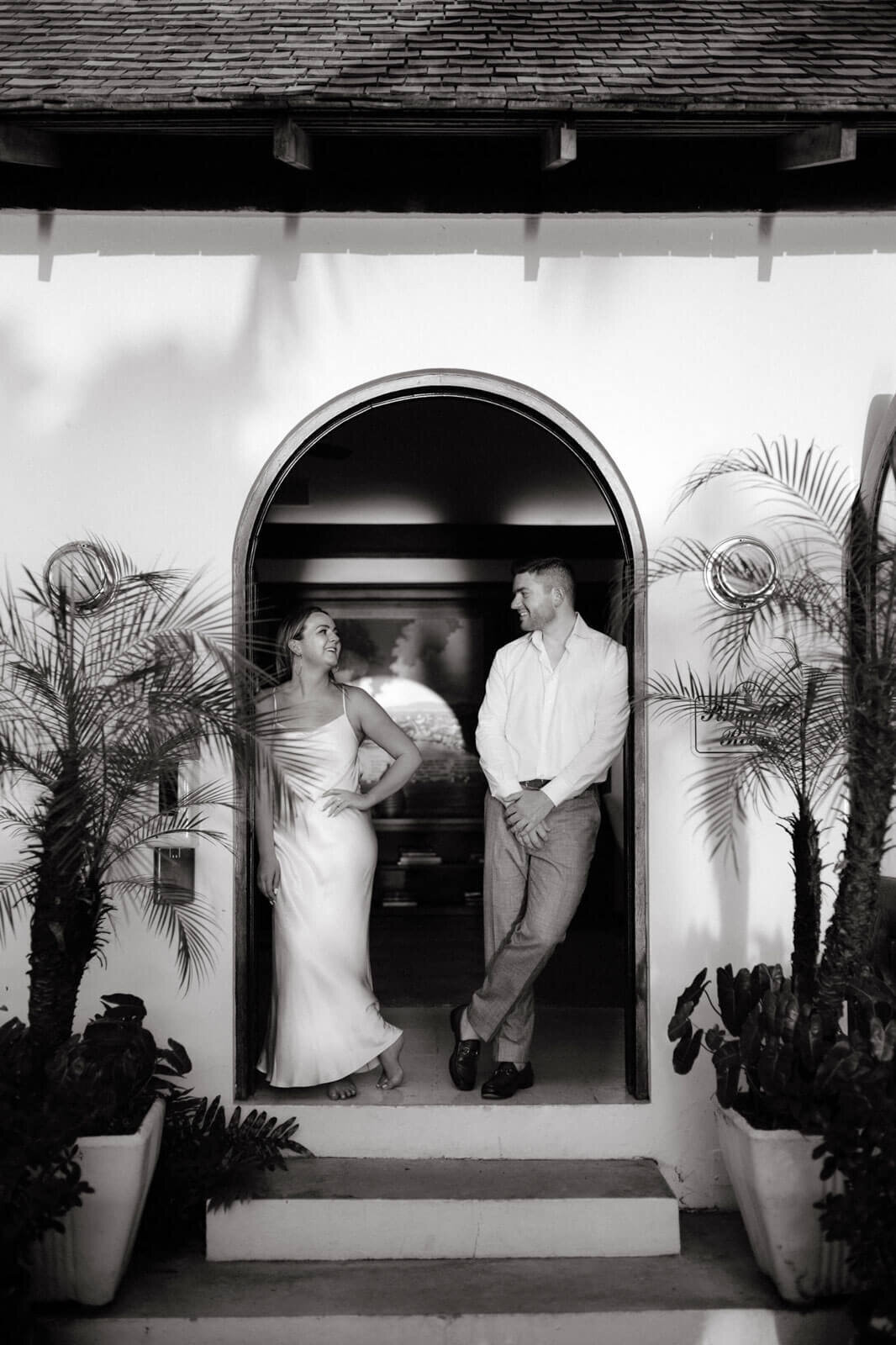 A Black and white photo of the engaged couple, facing each other, standing at the door of a villa at Round Hill Hotel, Jamaica.
