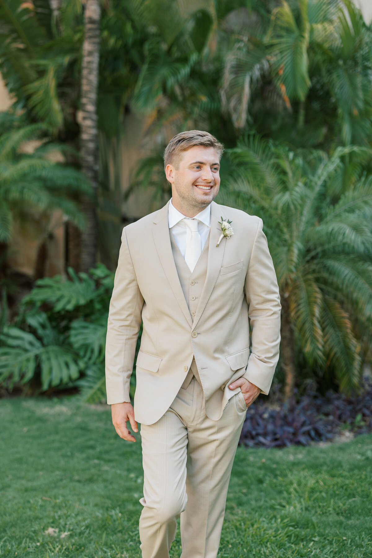 Groom walking confidently at Cancun resort in tan wedding suit, photographed by Philadelphia pro.