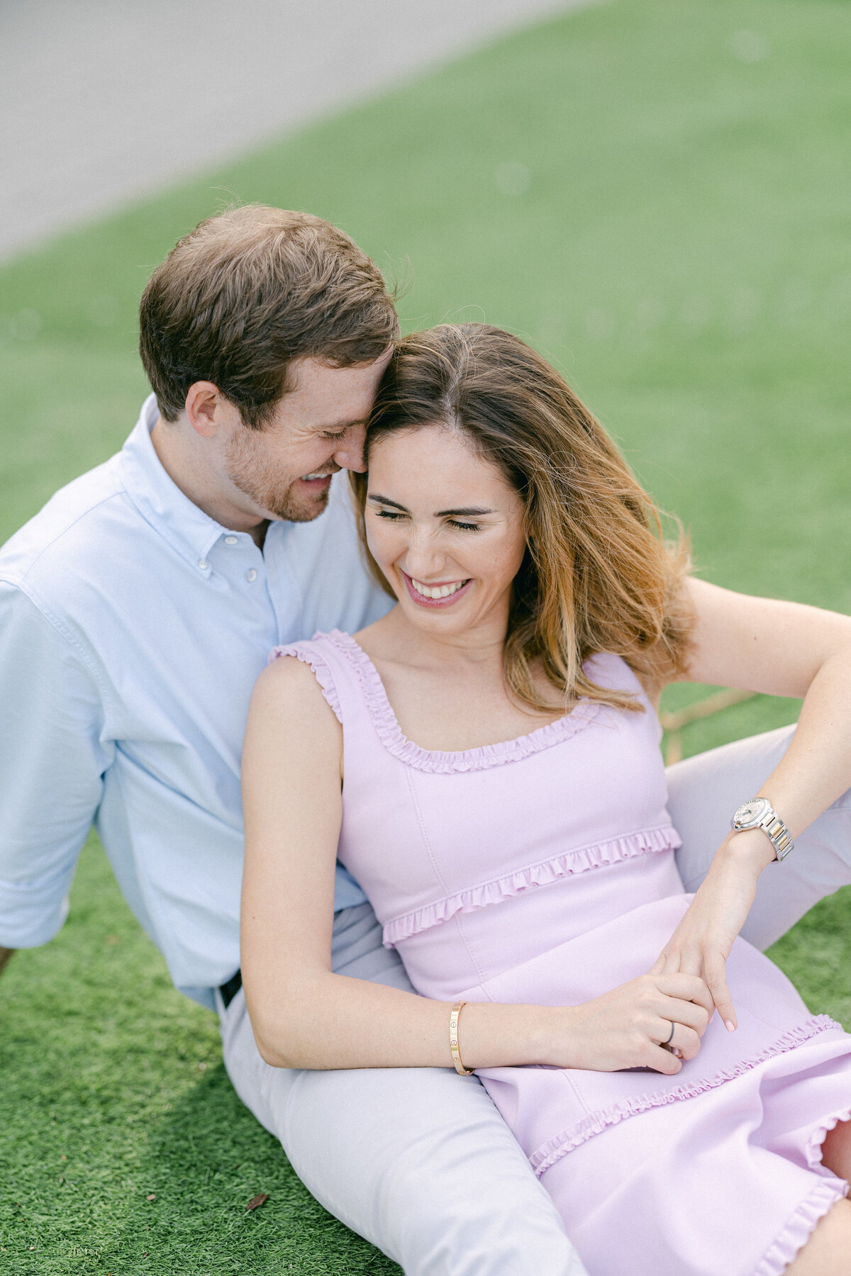 Engaged couple sitting on the grass, laughing and enjoying a tender moment together in Miami, photographed by Rodrigo Varela Photography.