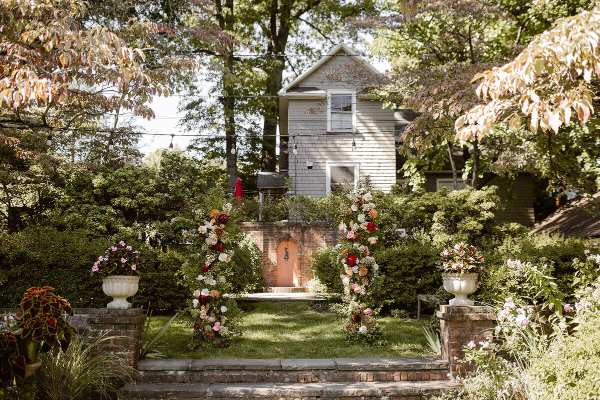 An intimate garden wedding ceremony setup, featuring lush floral arrangements and a picturesque backdrop of greenery and a charming house.