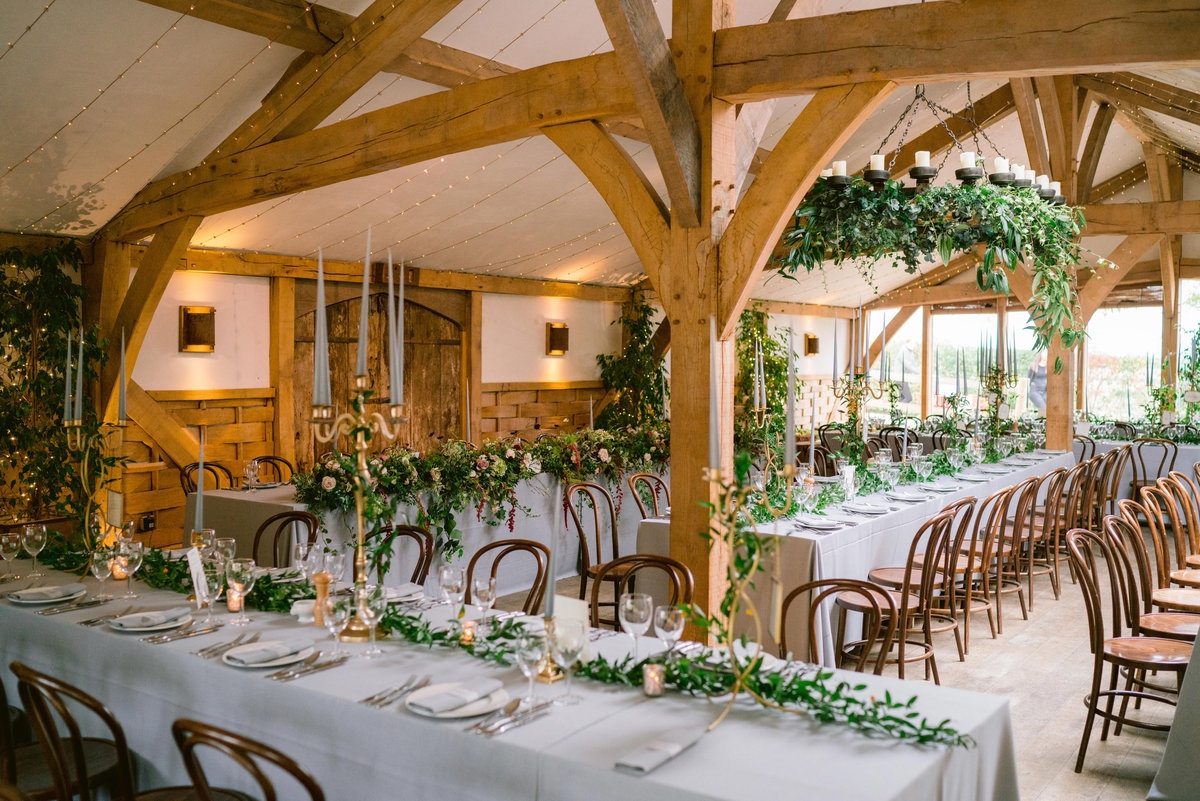 cripps barn wedding reception room laid out for the wedding breakfast with rustic flowers and hanging floral decor