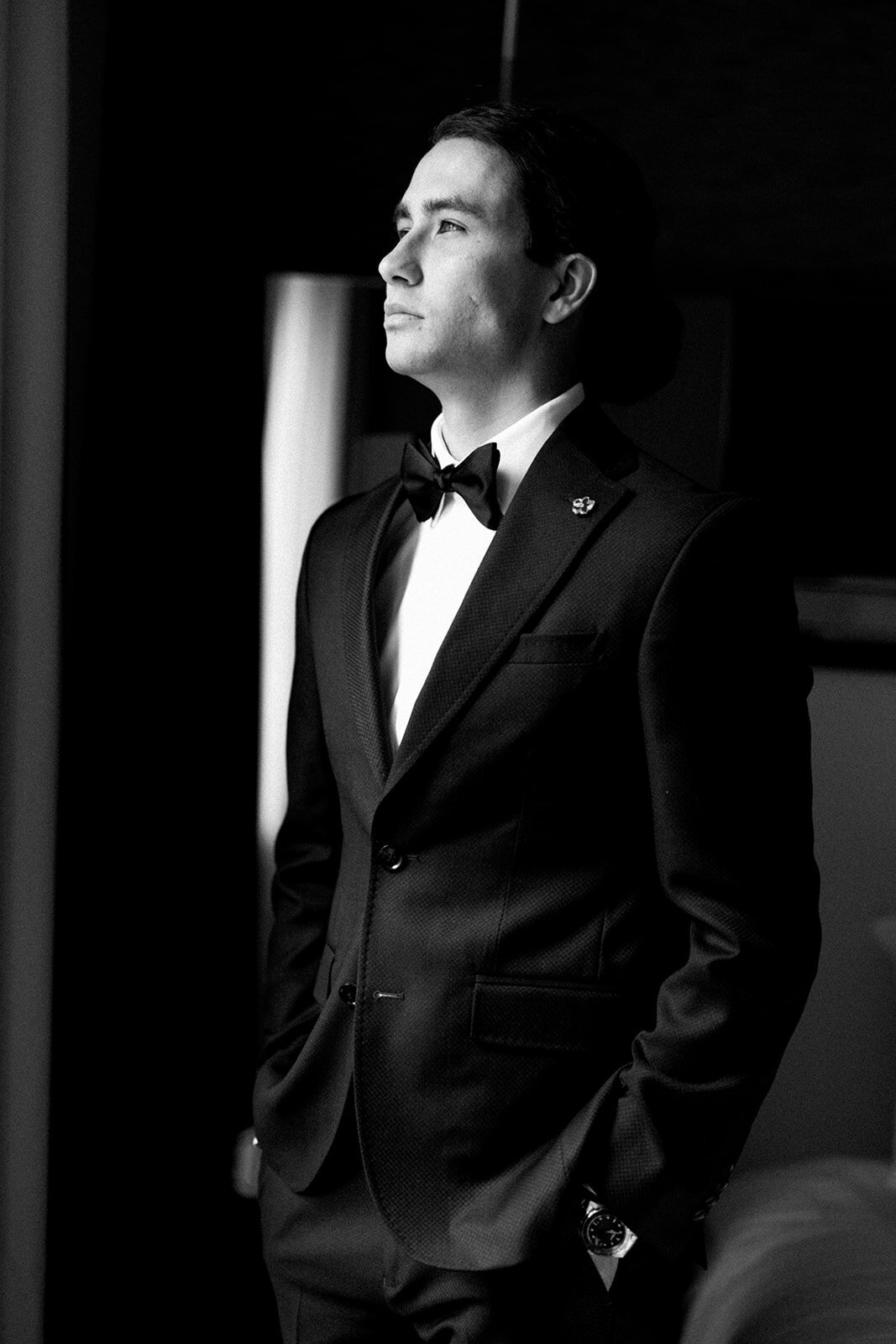 Wedding Photography, black and white image of groom looking out a window with his hands in his pockets