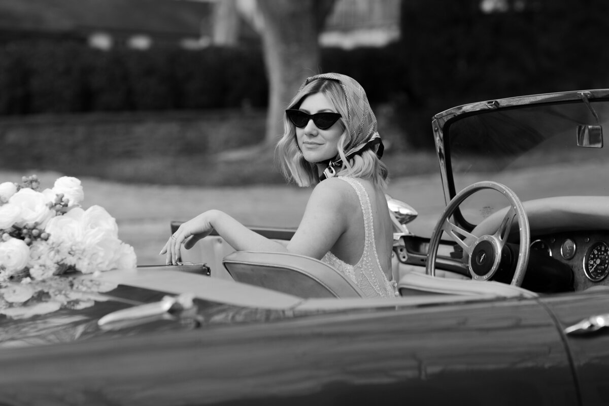 bride in headscarf and sunglasses sitting in convertible car