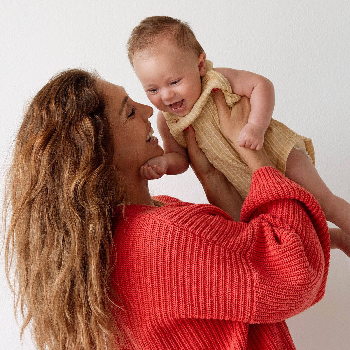 Mother smiling and lifting her newborn baby during a cozy lifestyle newborn photoshoot in Orange County.