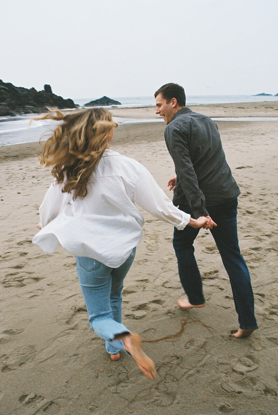 A couple holding hands and running on the beach. 