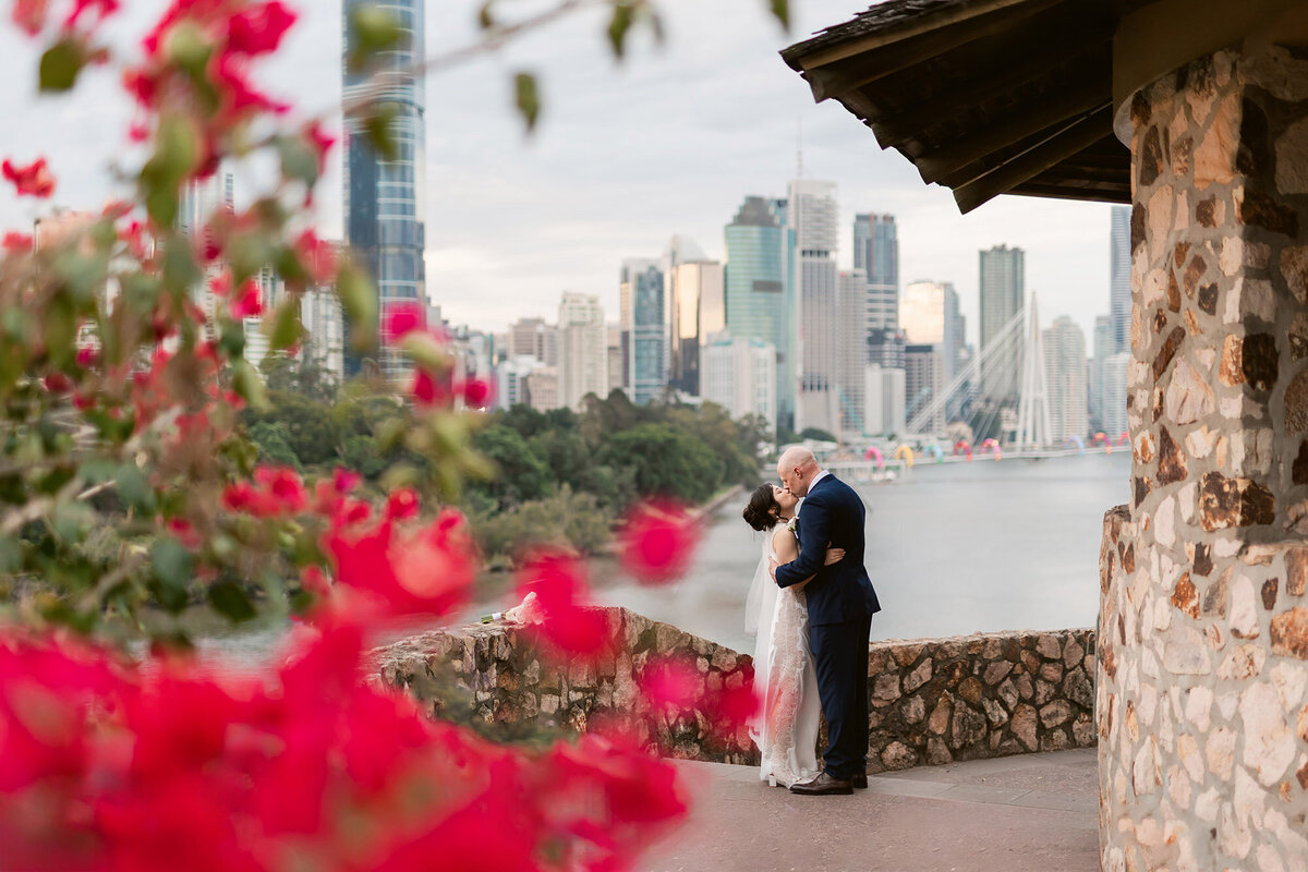 Brisbane wedding photographer captures newlyweds kissing at Kangaroo Point Cliffs with city skyline in the background
