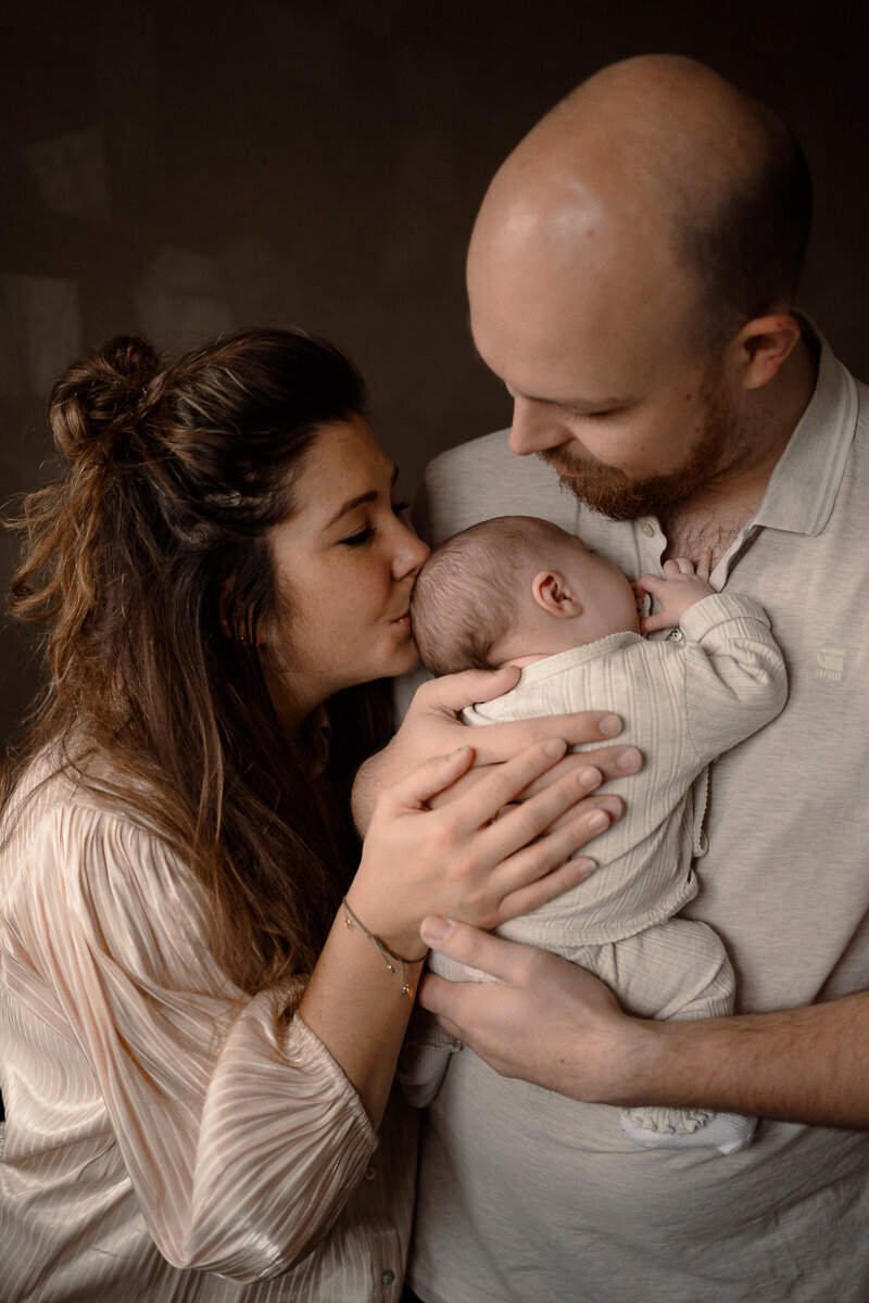 Vader houdt pasgeboren baby vast en moeder geeft baby een kusje op het hoofd