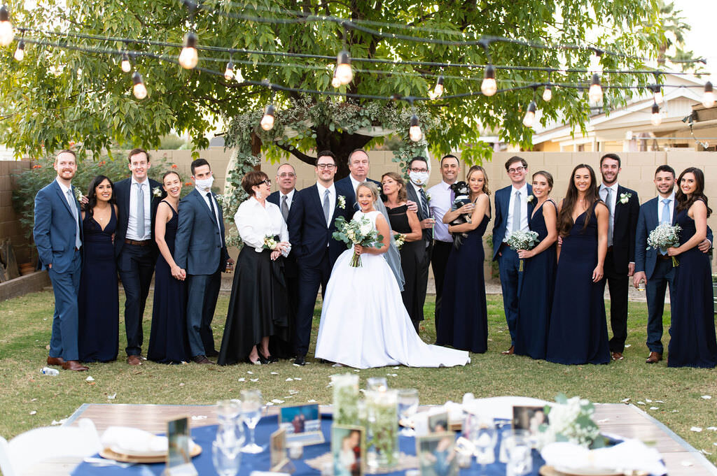 Bride and groom standing with their wedding party in a small backyard area.
