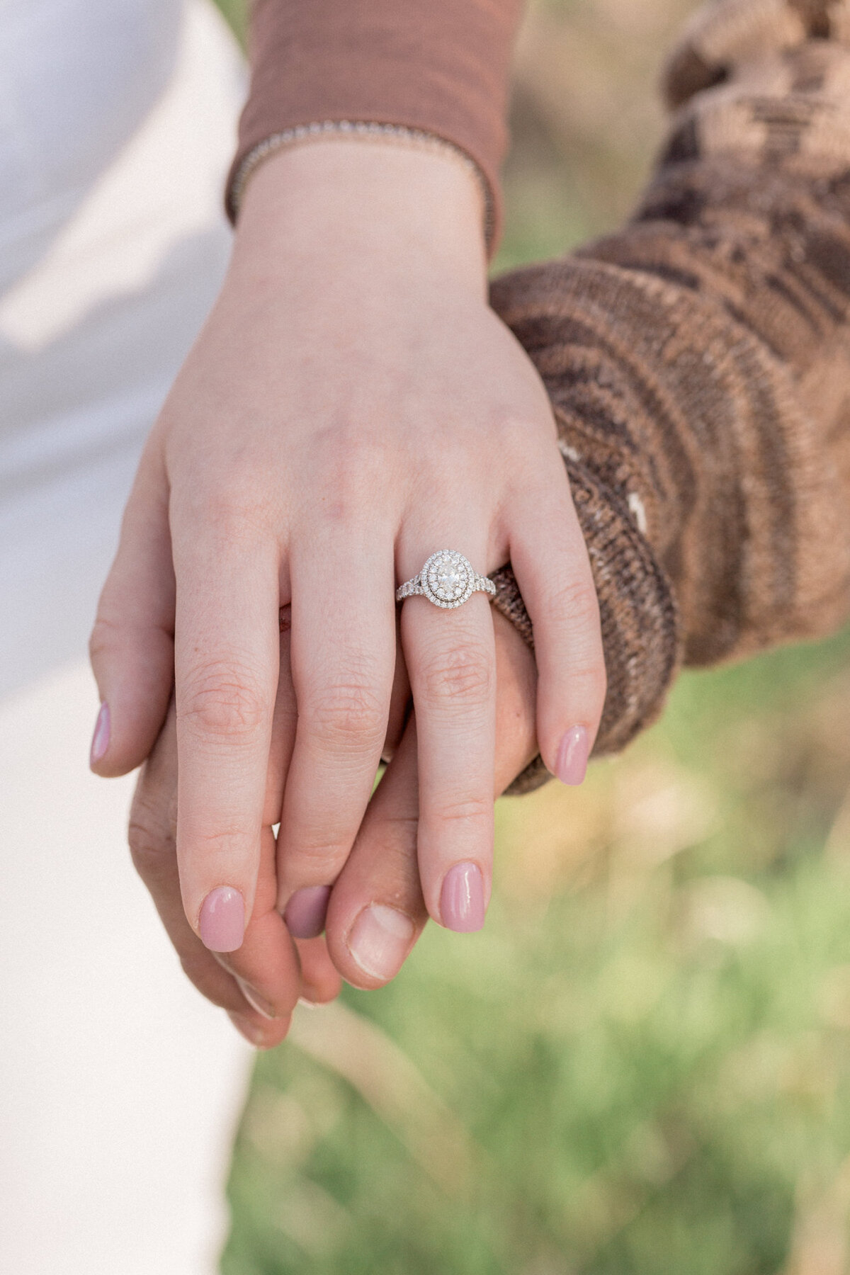 A couple hold hands, while their photographer captures a close up ring photo.