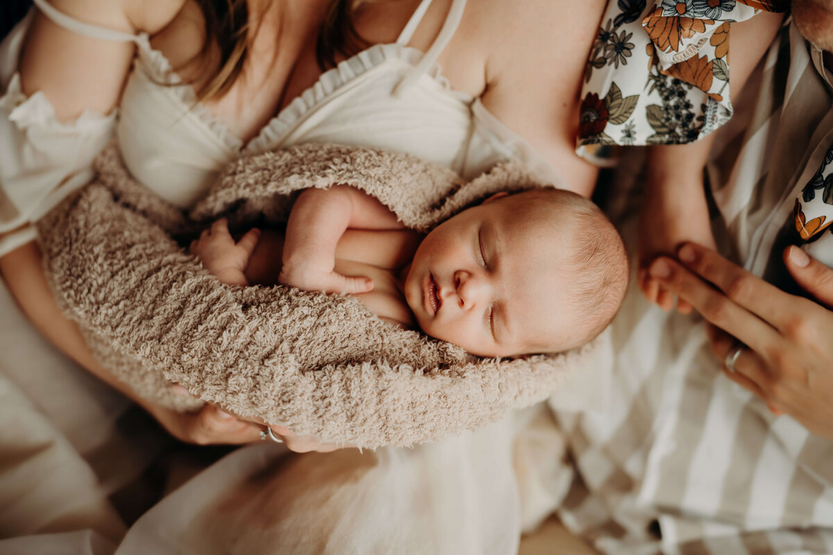 newborn boy wrapped in luxury blanket sleeps in his moms arms while dads hand holds his big sisters toes