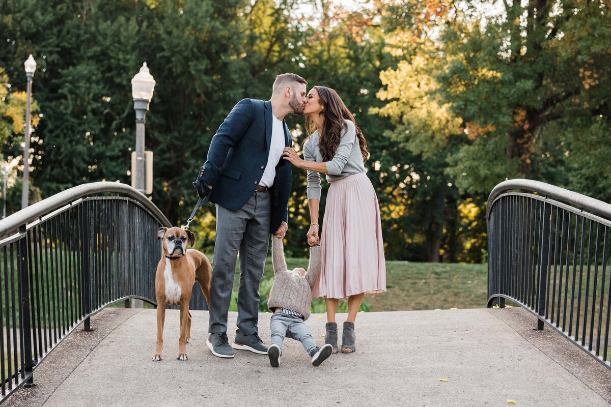 A Pittsburgh family photographer captures a couple kissing on a bridge while walking with their toddler and dog.