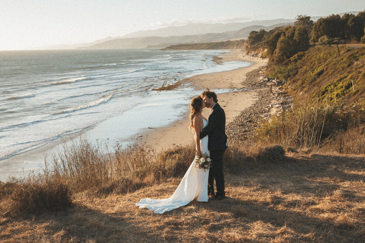 a bride and groom standing on a cliff edge overlooking the beach in santa barbara california at dp orchid farm wedding venue