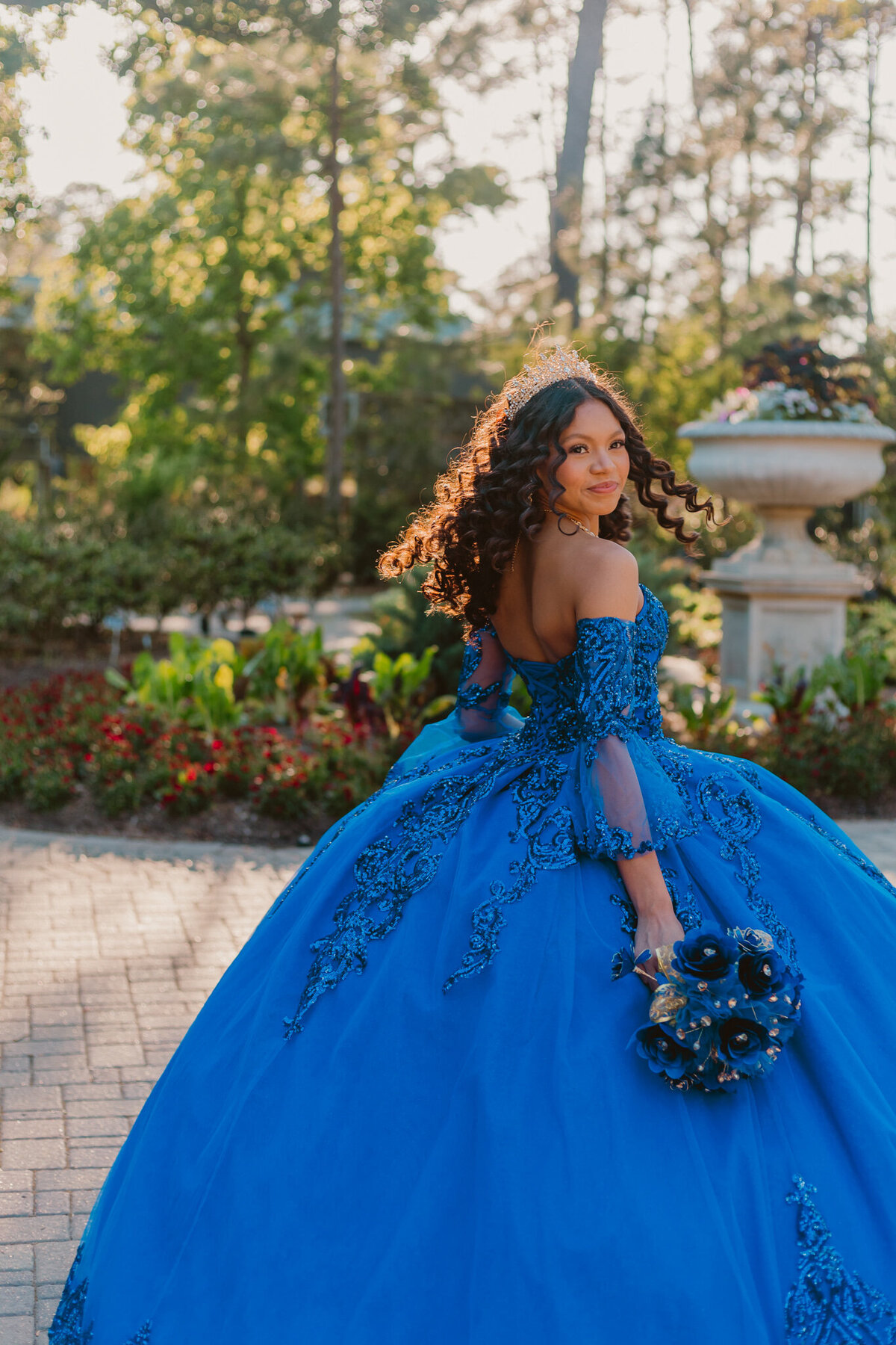 Stunning quinceañera portrait at Mercer Botanical Gardens, Houston. The young woman wears a vibrant blue ball gown, holding a matching bouquet, standing in a beautifully landscaped garden. Captured by ShutterUp Photography, Houston quinceañera and event photographer.