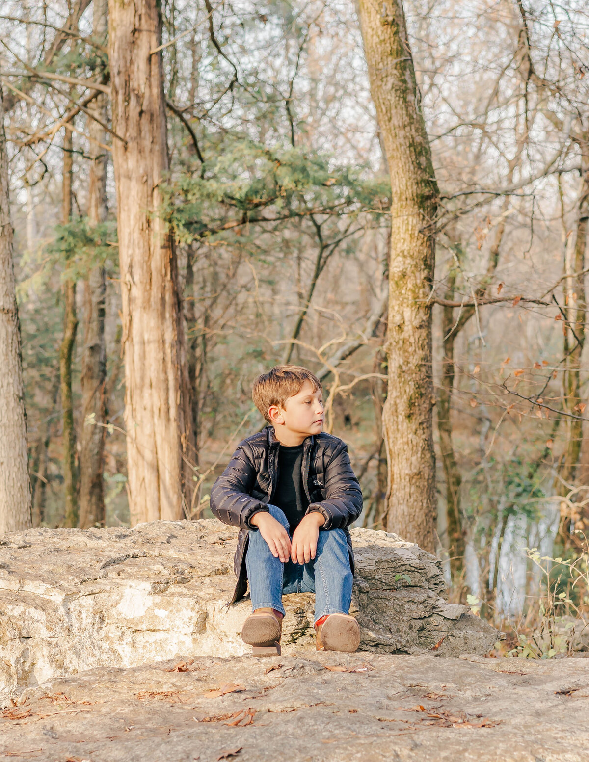 little boy sitting on rock in the woods on the stones river in rutherford county Tennessee