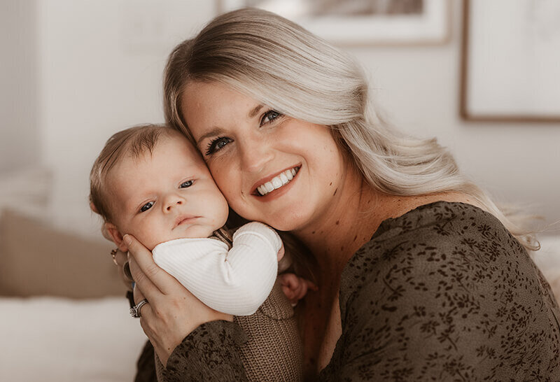 mom closely embraces newborn baby holding her cheek close to hers.
