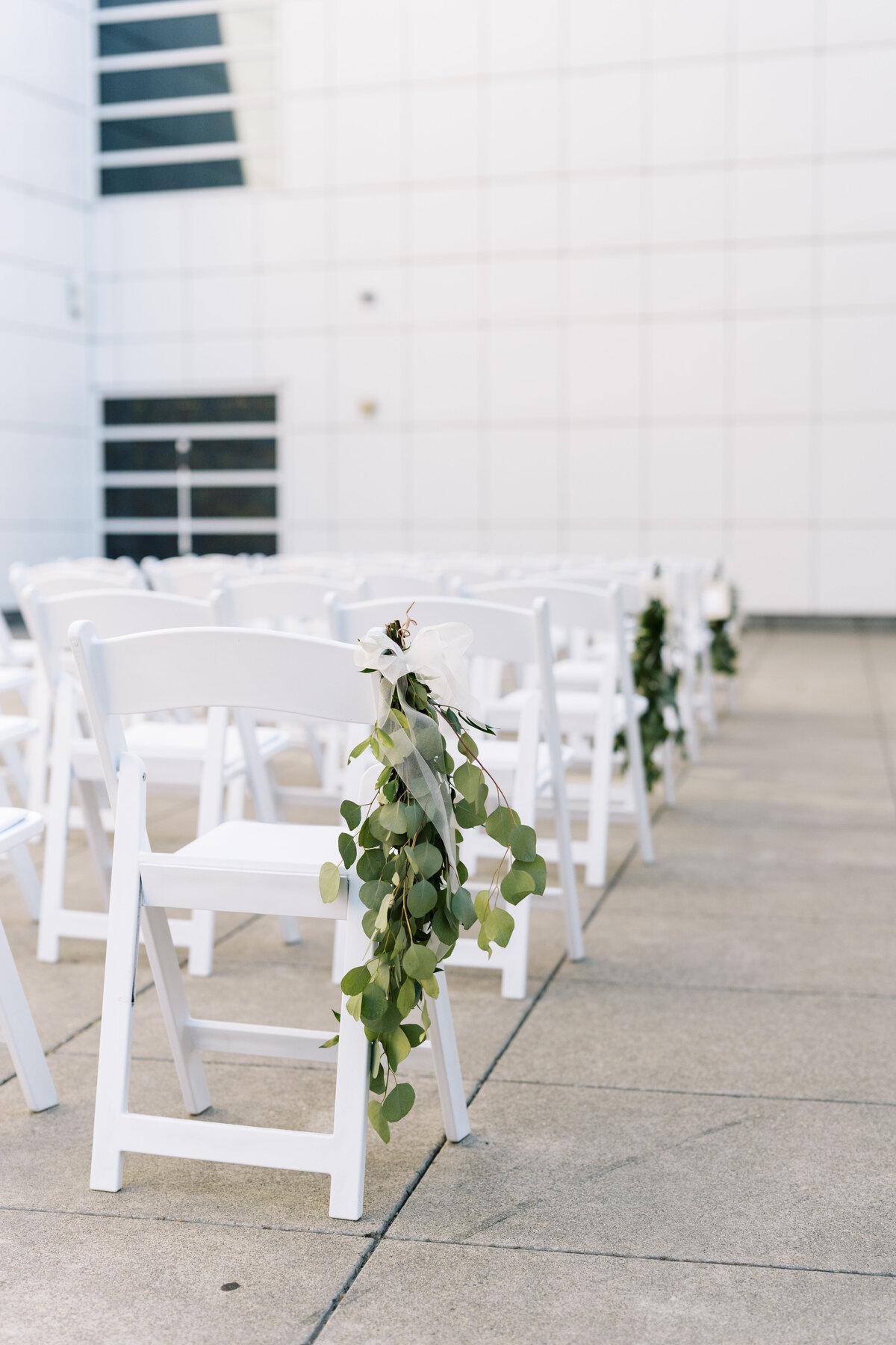 white ceremony chairs with greenery tied to them