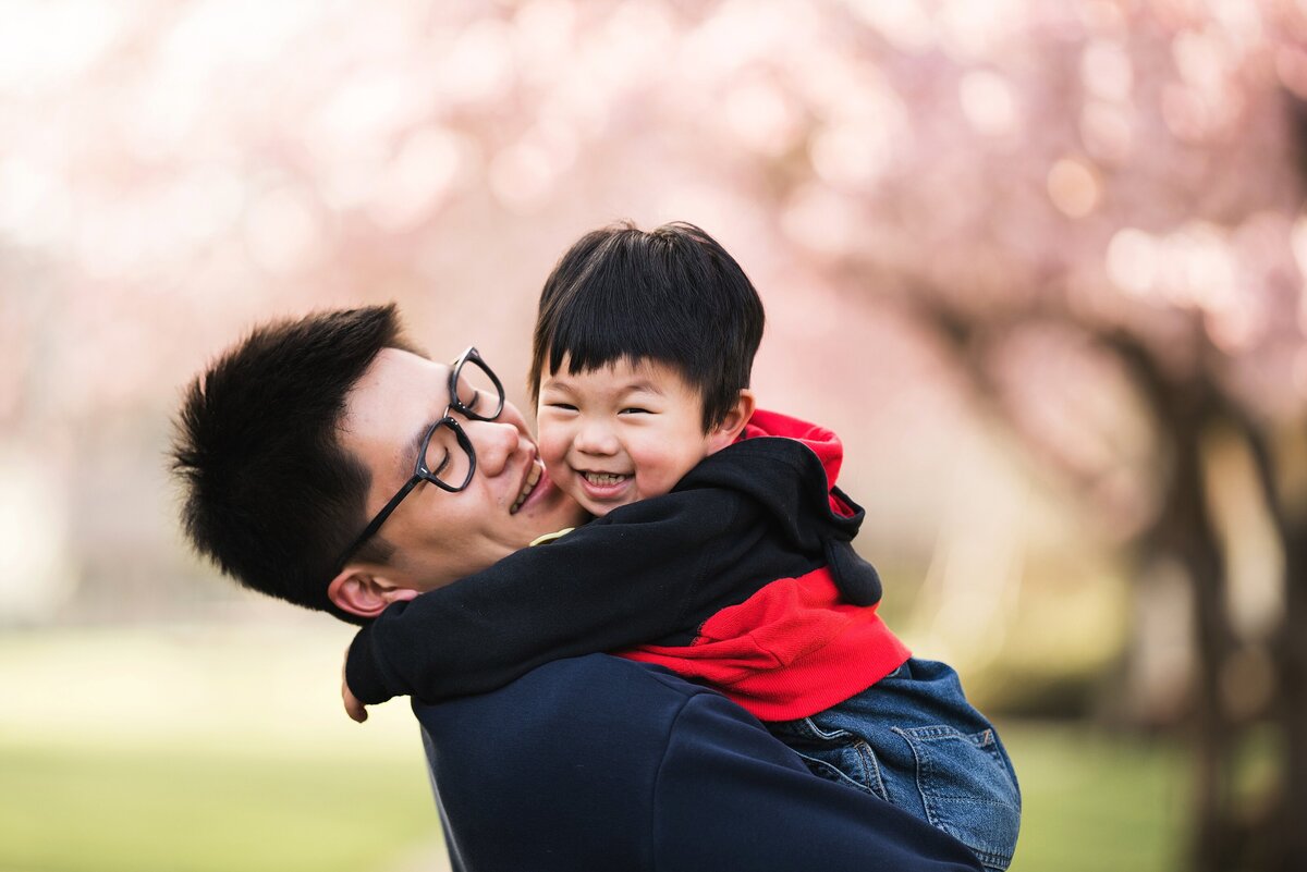 Asian father and son smiling with cherry blossoms in the background