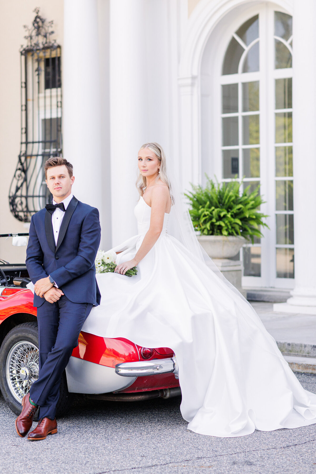 Bride and groom staring at the camera while posing with a vintage car during their Tupper Manor wedding portraits