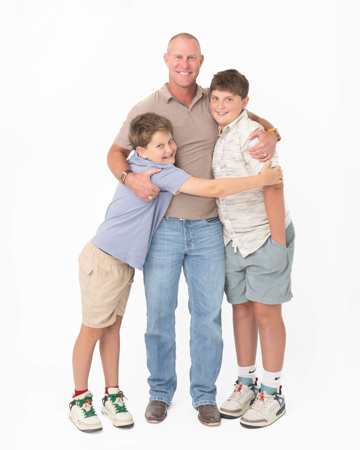 studio portrait on white backdrop of a cool dad hugging and pulling in his elementary aged boys