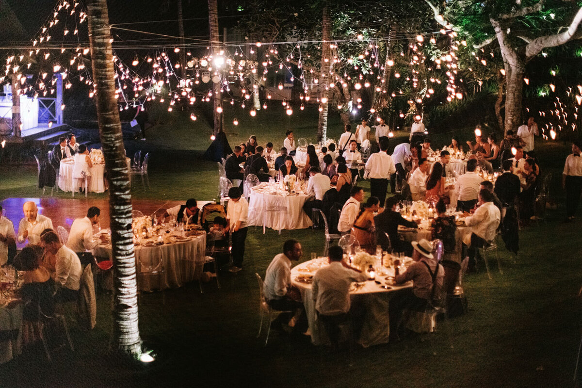 The guests are seated in an outdoor wedding reception, with fairy lights, in Khayangan Estate, Bali, Indonesia. Image by Jenny Fu Studio