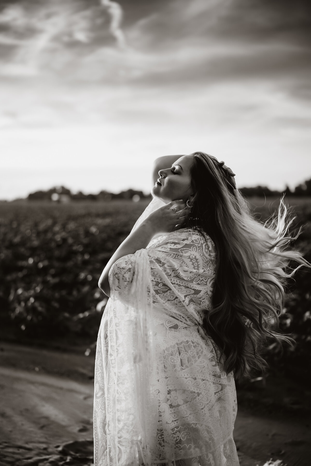 black and white dramatic portrait of a pregnant women in a  boho lave maternity gown flipping her hair in a field