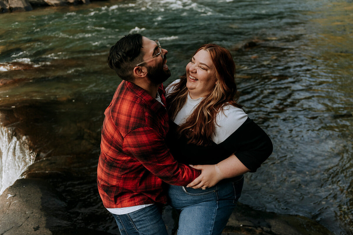 Newly engaged couple laughs next to Whistler waterfall after their proposal