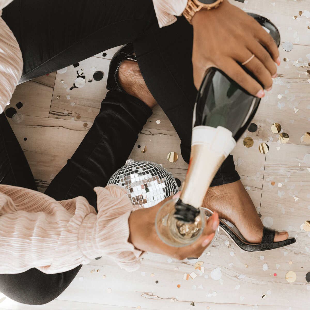 Closeup of a woman’s arm while sitting on the floor pouring a flute of champagne