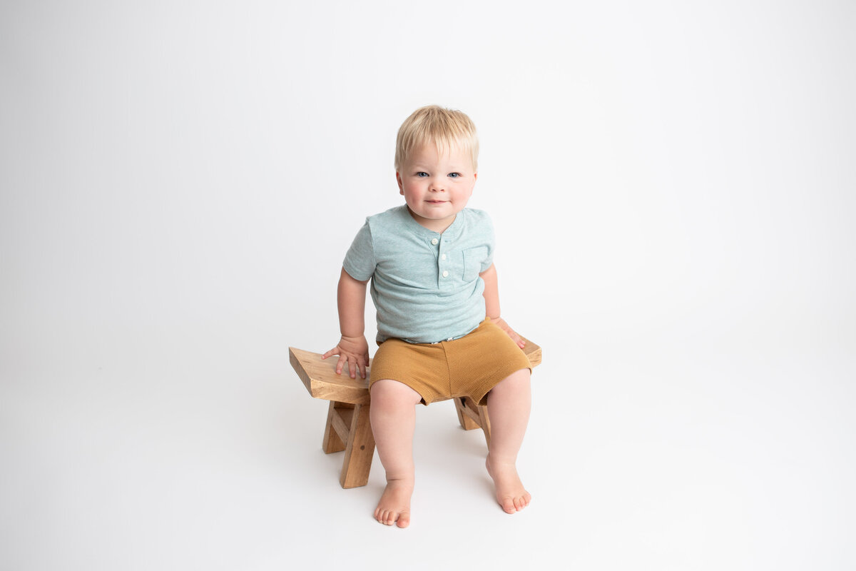 Little boy sitting on a wooden stool with a plain white backdrop