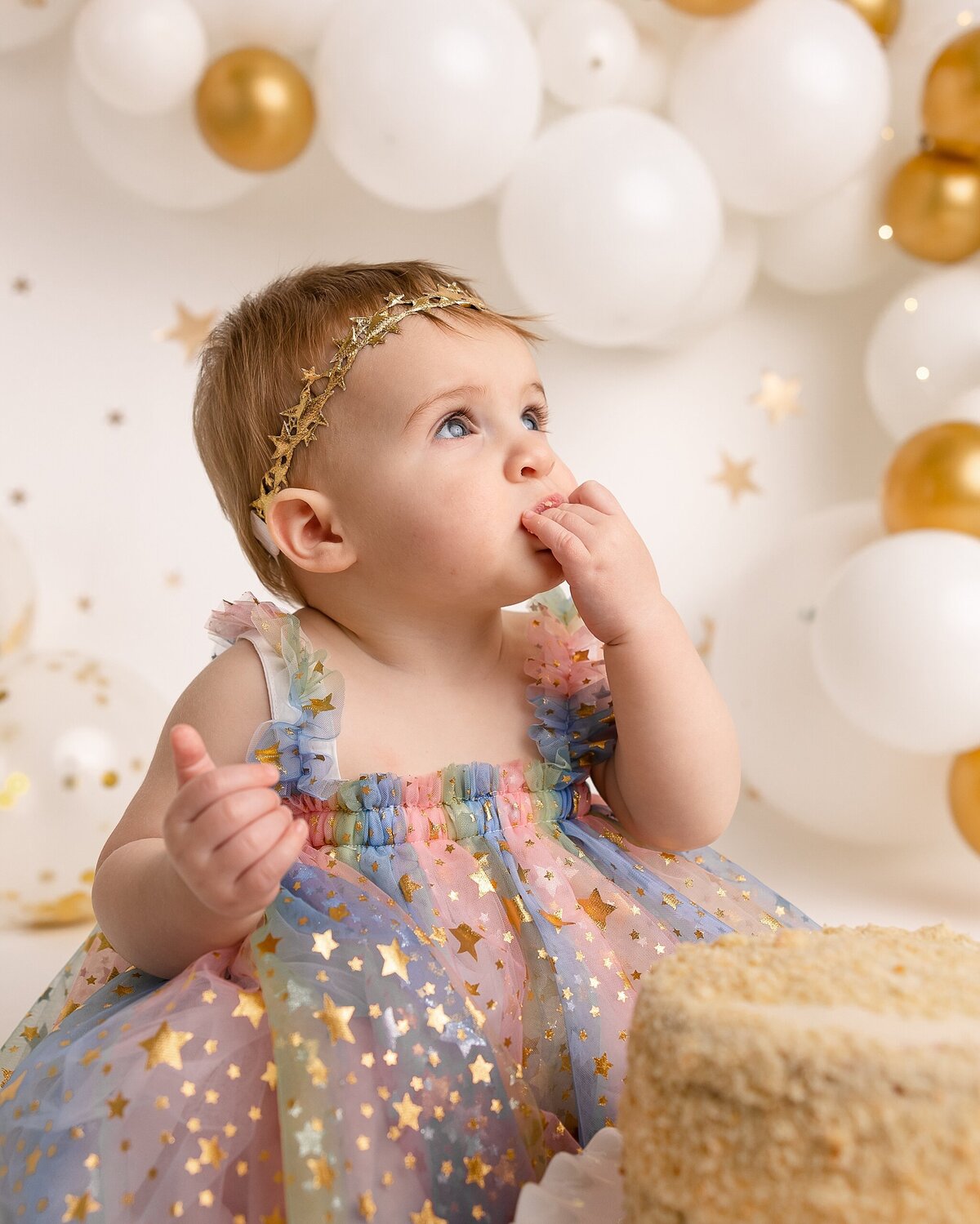 baby eating cake for first birthday in rainbow dress