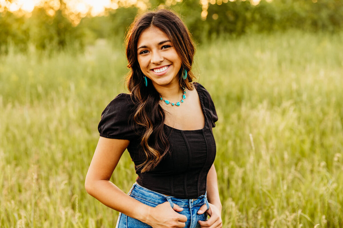 gorgeous senior posing with her thumbs in her belt loops at sunset