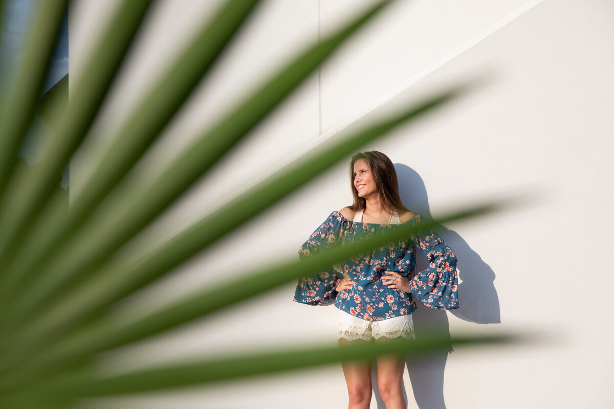 A girl leaning on a wall seen through a palm frawn