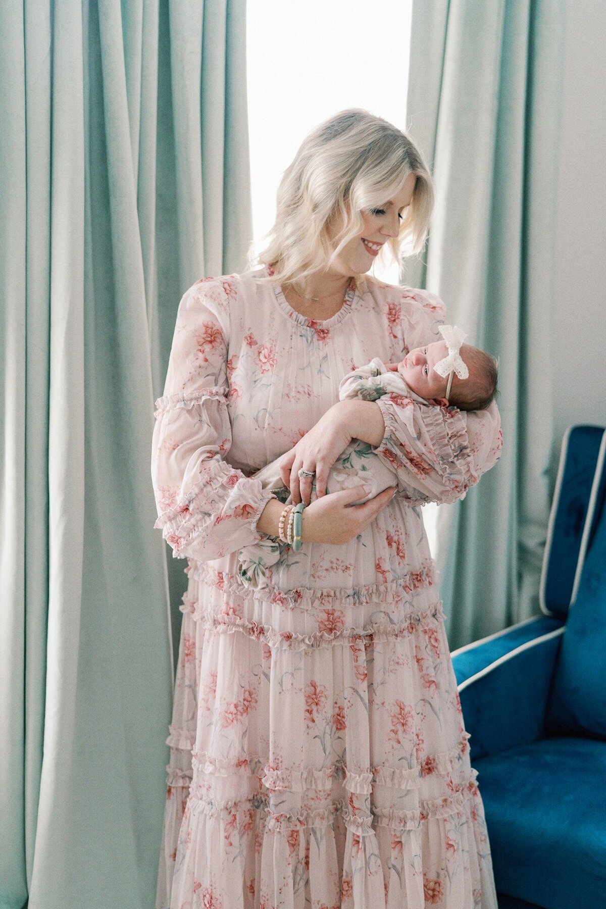 mom-in-pink-dress-holding-newborn-in-nursery