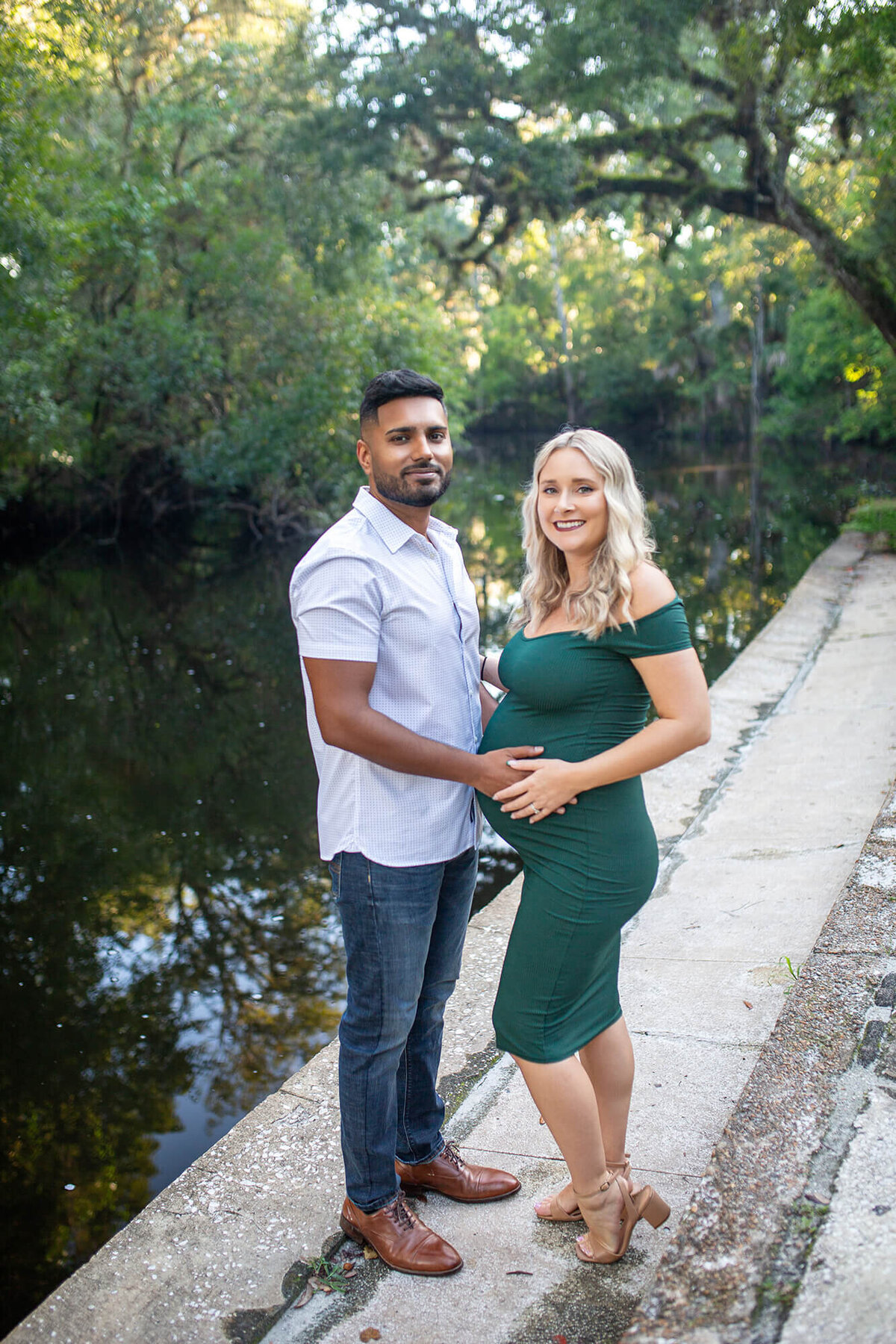 Man and woman with hands on pregnant belly standing by Hillsborough River 