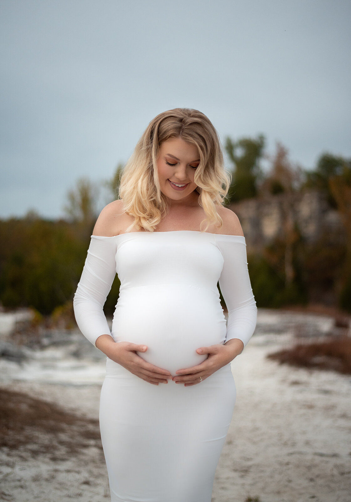 pregnant mom holding her belly outside wearing a white dress by st. louis maternity photographer, sutherland photography