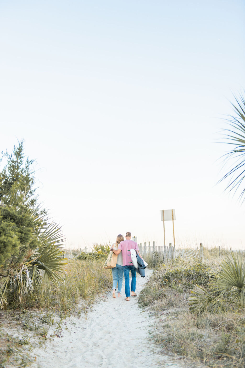 Couple walking down a path to the beach holding a surfboard