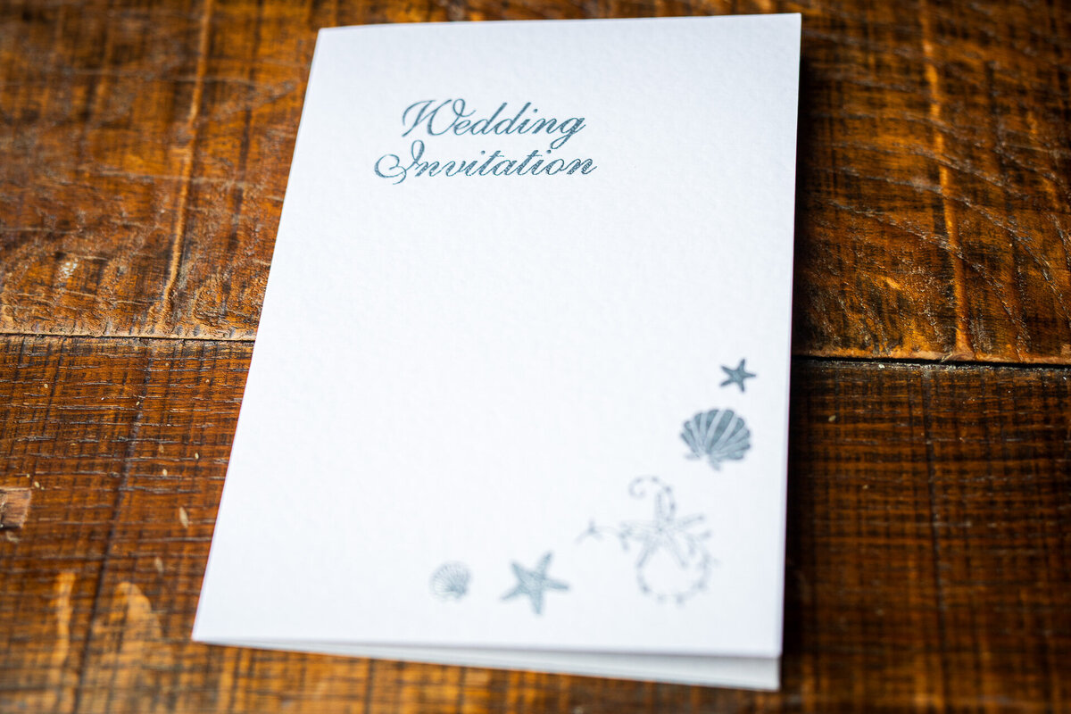 White and silver wedding invitation featuring embossed shells