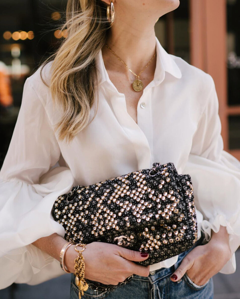 Female model wearing white button down shirt, gold jewelry and carrying a beaded Chanel clutch