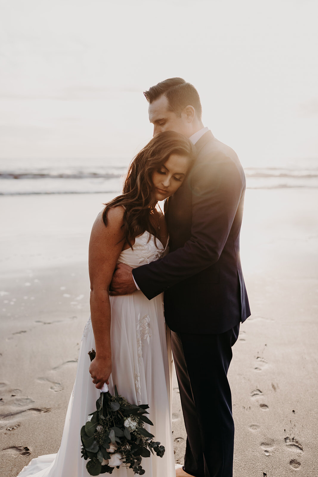 a bride nestling into the groom's shoulder as the sunsets behind them
