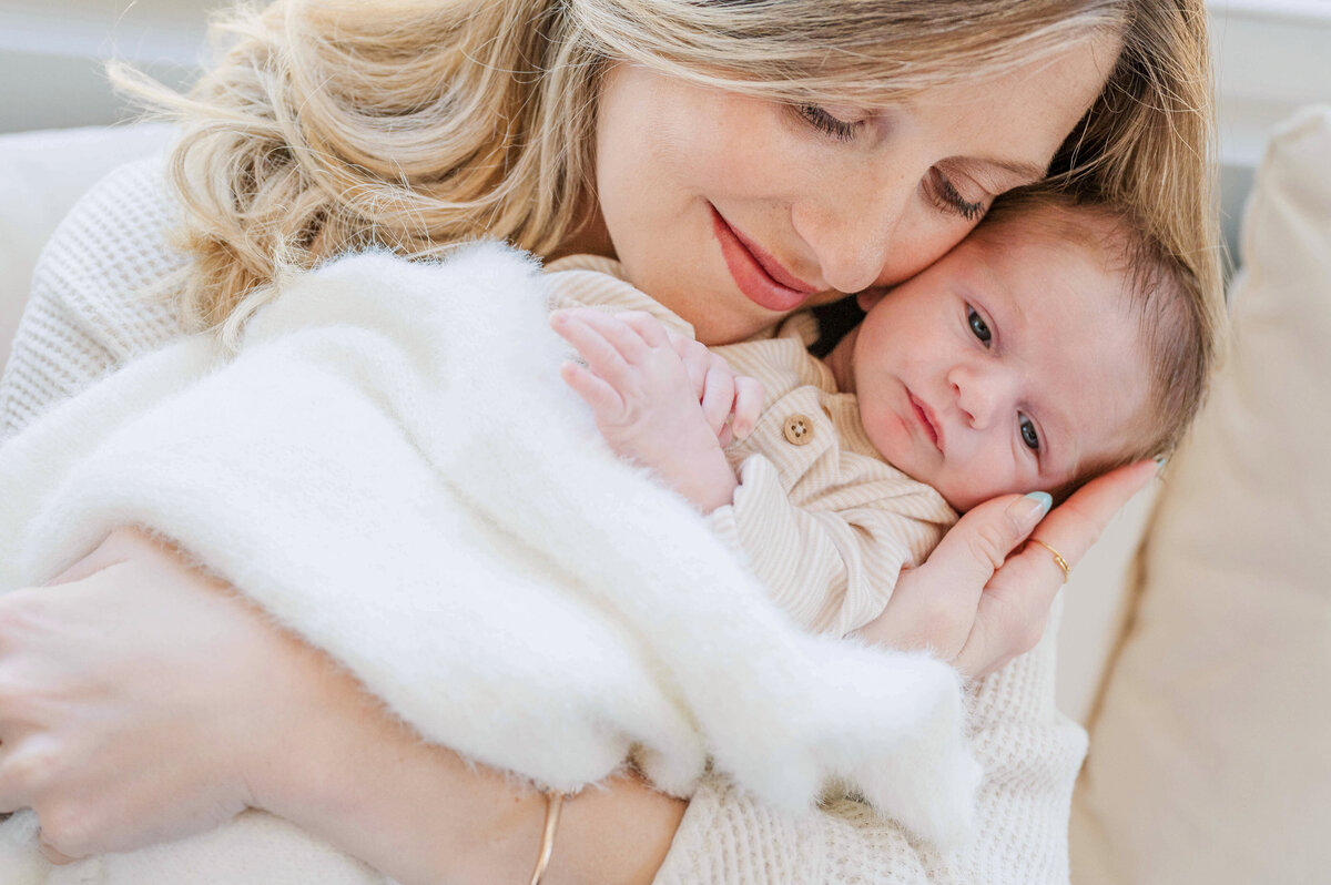 A sweet blond mom gently holding her newborn baby to her cheek.