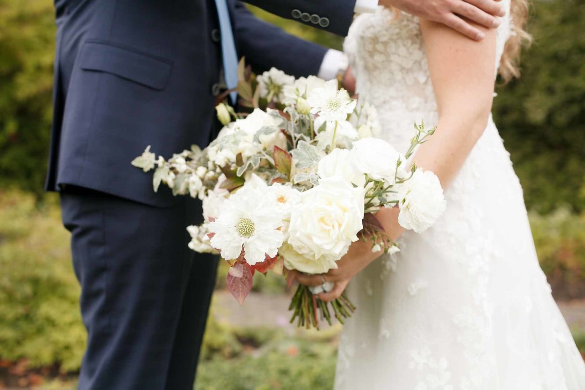 bride holding a bouquet of white fall flowers, dahlias, roses, scabiosa, with rust and silver fall foliage