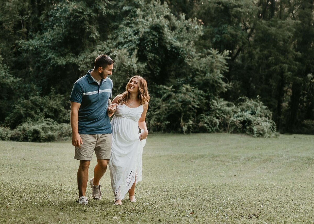A couple walking through a grassy field during their maternity session captured by a Pittsburgh maternity photographer.