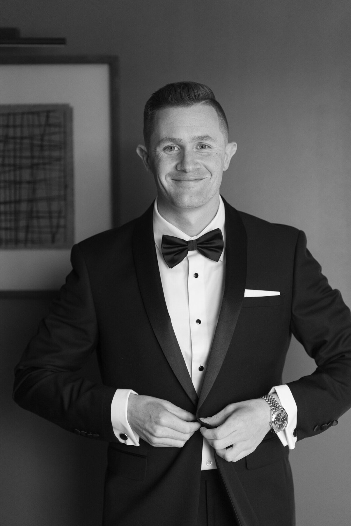 Groom adjusting tuxedo jacket in black and white portrait before ceremony