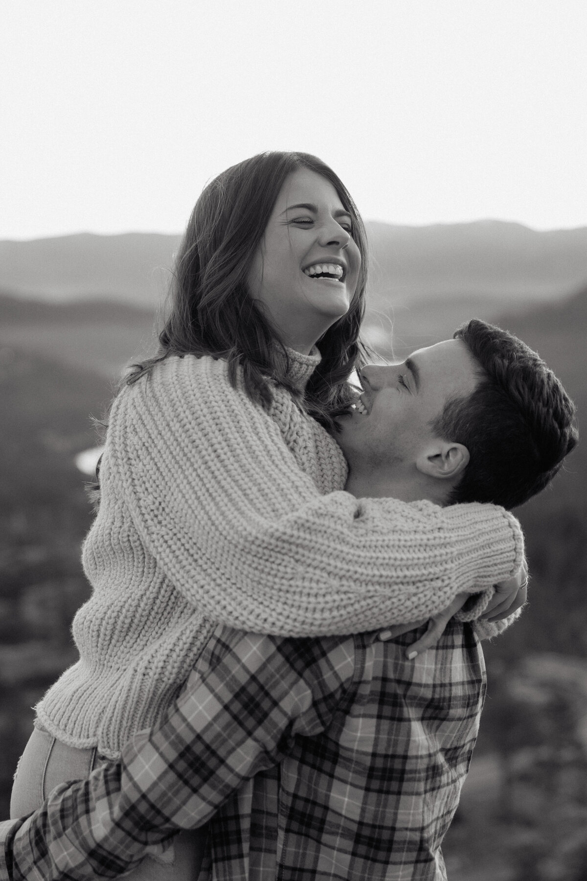 A couple sits atop a scenic overlook, basking in warm sunlight and sharing a moment of connection.