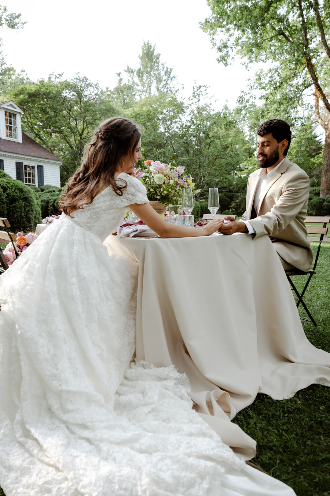 Bride and groom sharing a quiet moment at a table set up in a garden, surrounded by spring greenery.